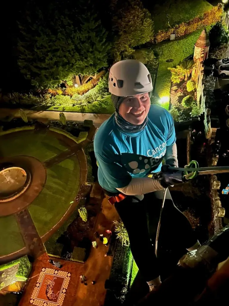 A woman abseiling down Belfast Castle wearing a Cancer Focus NI t-shirt.