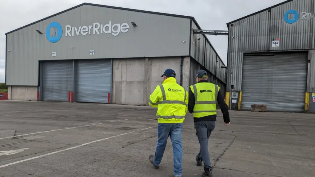 Two men in high-vis jackets walking towards an industrial warehouse building with the logo 'RiverRidge'