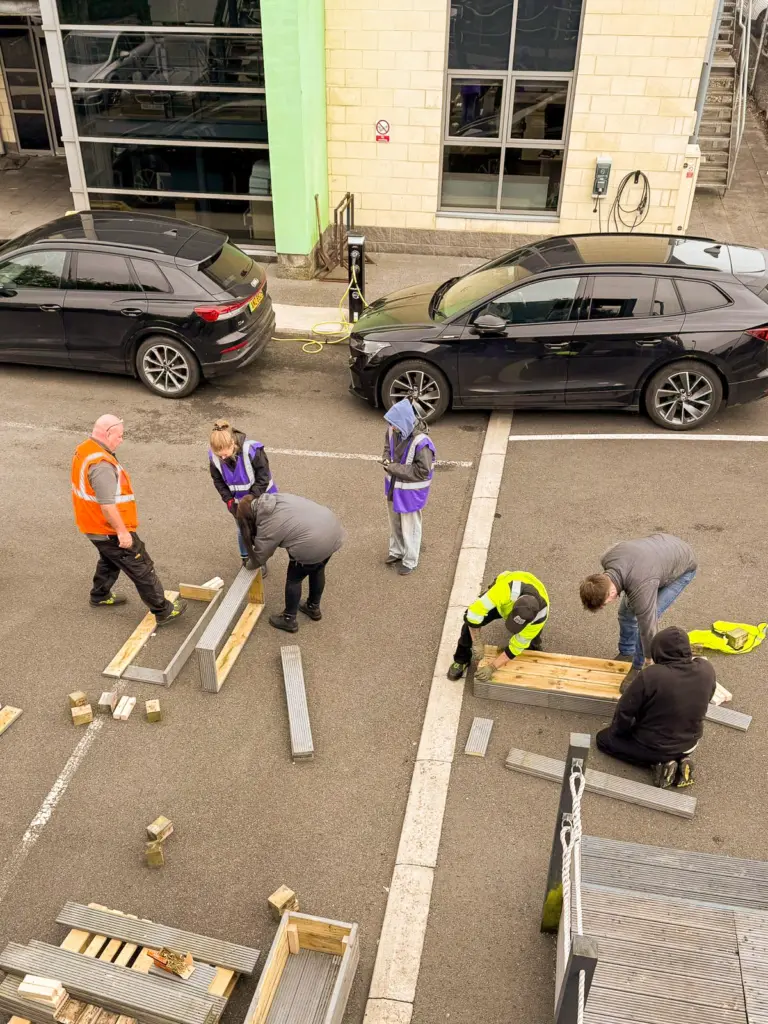 Several people wearing high-vis vests constructing planters out of wooden planks in a car park.